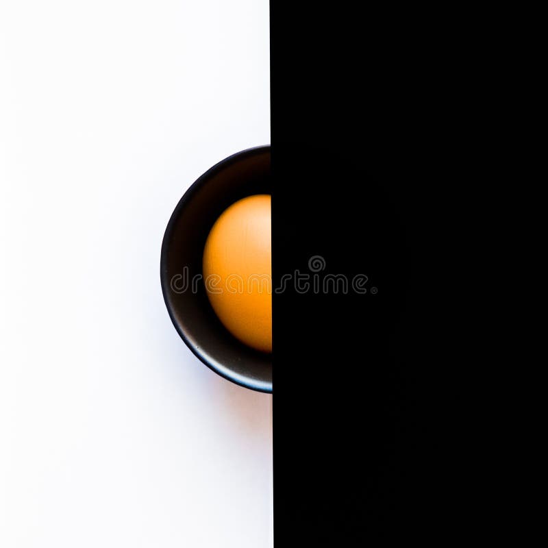 Hälfte des orange Eies innerhalb der schwarzen Schüssel auf dem weißen Hintergrund auf dem linken und schwarzen Hintergrund auf d stockbild Hälfte des orange Eies innerhalb der schwarzen Schüssel auf dem weißen Hintergrund auf dem linken und schwarzen Hintergrund auf d stockbild