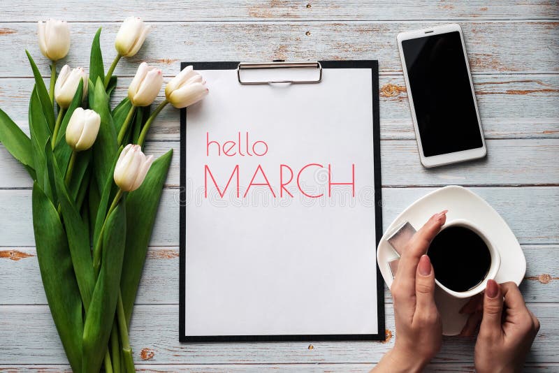 Greeting card with the inscription Hello March. Bouquet of white Tulip flowers with a Cup of coffee and a smartphone on a wooden background. Greeting card with the inscription Hello March. Bouquet of white Tulip flowers with a Cup of coffee and a smartphone on a wooden background
