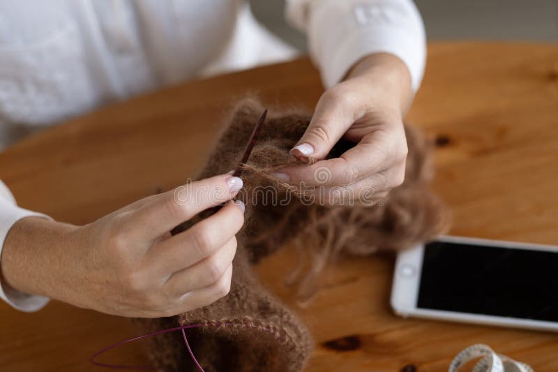 Woman&#x27;s hands knitting brown wool yarn pattern. Closeup horizontal photo. Freelance creative handicraft concept, hobby and lifestyle. Woman&#x27;s hands knitting brown wool yarn pattern. Closeup horizontal photo. Freelance creative handicraft concept, hobby and lifestyle