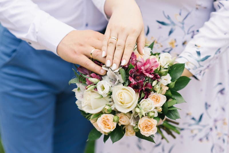 Hände der Braut und des Bräutigams mit Eheringen liegen auf dem Heiratsblumenstrauß von hellen Blumen lizenzfreie stockbilder Hände der Braut und des Bräutigams mit Eheringen liegen auf dem Heiratsblumenstrauß von hellen Blumen lizenzfreie stockbilder