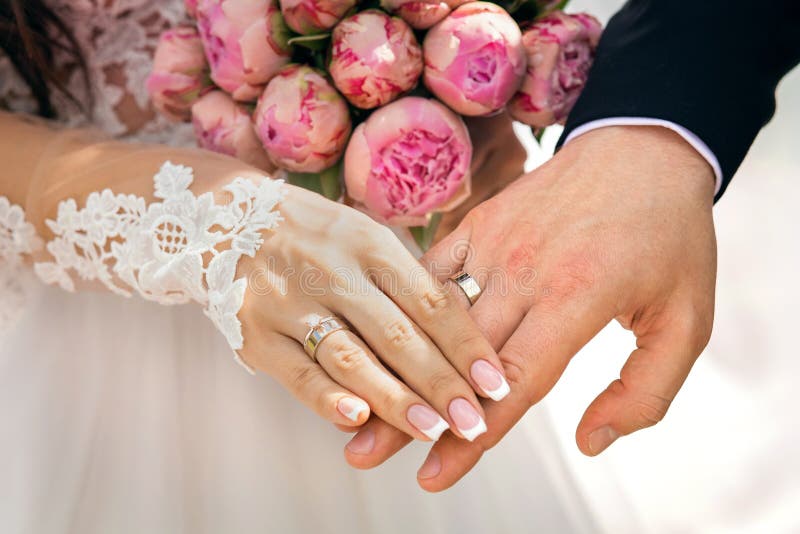 Hände der Jungvermählten mit Ringen auf den Fingern, nahe bei einem Blumenstrauß mit rosa Pfingstrosen, der Braut und den Bräutig lizenzfreies stockbild Hände der Jungvermählten mit Ringen auf den Fingern, nahe bei einem Blumenstrauß mit rosa Pfingstrosen, der Braut und den Bräutig lizenzfreies stockbild