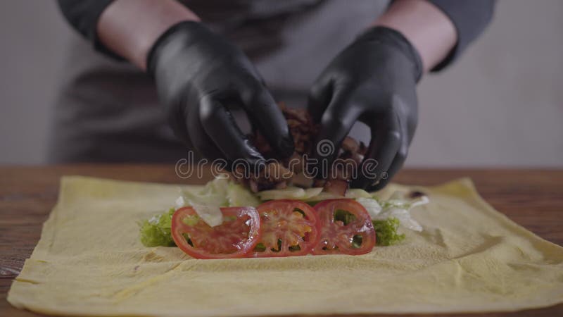 Hände des Chefs in den schwarzen Küchenhandschuhen, die shawarma Nahaufnahme machen Der Koch, der Fleisch, Tomaten und Zwiebel au