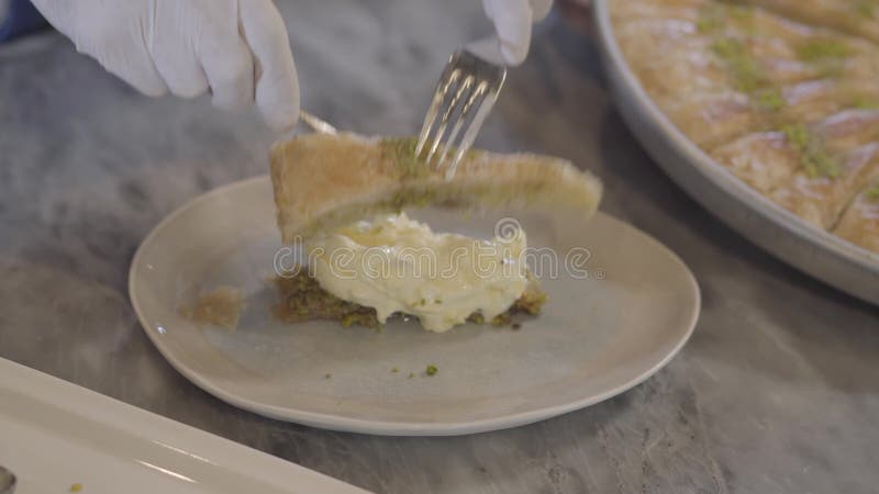 Hände des Chefs in den weißen Gummihandschuhen, die das östliche süße kunafa aufstellt geschmolzenen Käse innerhalb des Abschluss