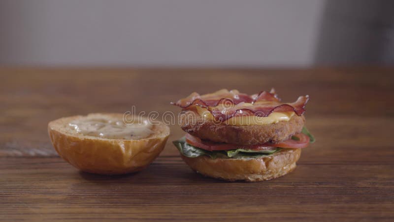 Hände des Chefs, der Burgernahaufnahme macht Der Koch, der becon und Zwiebel auf das Kotelett, die Tomatenscheiben und die Basili