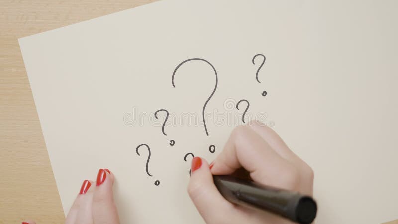 Hände einer Frau, die mehrfache Fragezeichen auf einem Weißbuch unter Verwendung einer schwarzen Markierung zeichnet -
