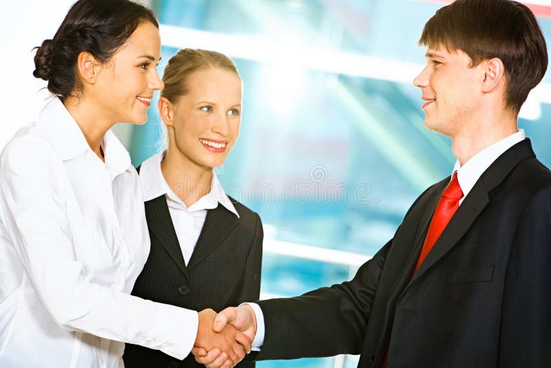 Photo of two business partners shaking hands after signing contract in the office with their colleague near by. Photo of two business partners shaking hands after signing contract in the office with their colleague near by