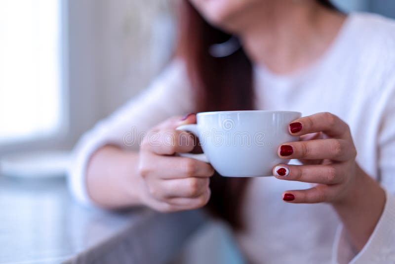 Händer för modell för Closeupskönhetstående med rött mode spikar att måla i den varma tröjan som rymmer en vit kopp kaffe, te, mj arkivfoton Händer för modell för Closeupskönhetstående med rött mode spikar att måla i den varma tröjan som rymmer en vit kopp kaffe, te, mj arkivfoton