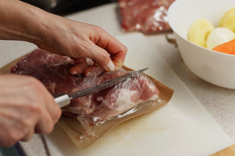 Händerna på kvinnan som håller på att öppna vakuumförpackningen med kött på en plaststyckningsdel arkivfoto