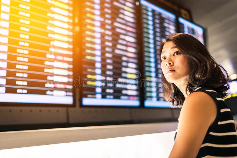 Härlig asiatisk kvinnahandelsresande på informationsskärmen om flyg i ett flygplats-, lopp- eller tidbegrepp, varm ljus effekt royaltyfria foton Härlig asiatisk kvinnahandelsresande på informationsskärmen om flyg i ett flygplats-, lopp- eller tidbegrepp, varm ljus effekt royaltyfria foton