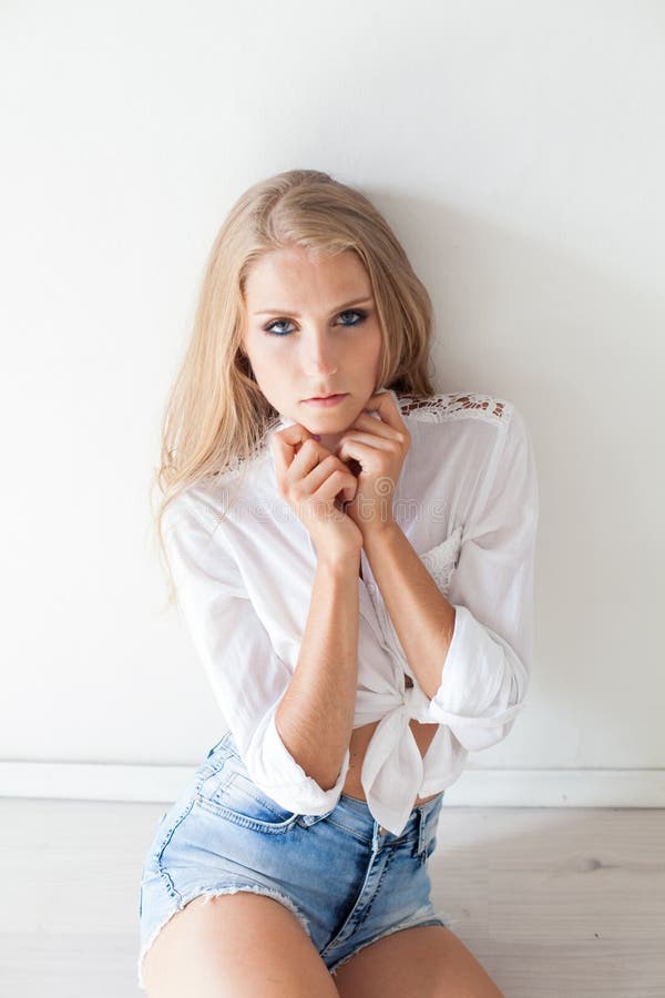 Beautiful blonde girl with blue eyes sitting on the floor in a white room. Beautiful blonde girl with blue eyes sitting on the floor in a white room