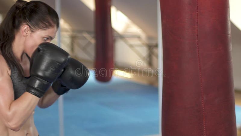 Härlig boxningkvinnautbildning med att stansa påsen i konditionstudio Våldsam styrka Kvinnligpassformkropp långsam rörelse