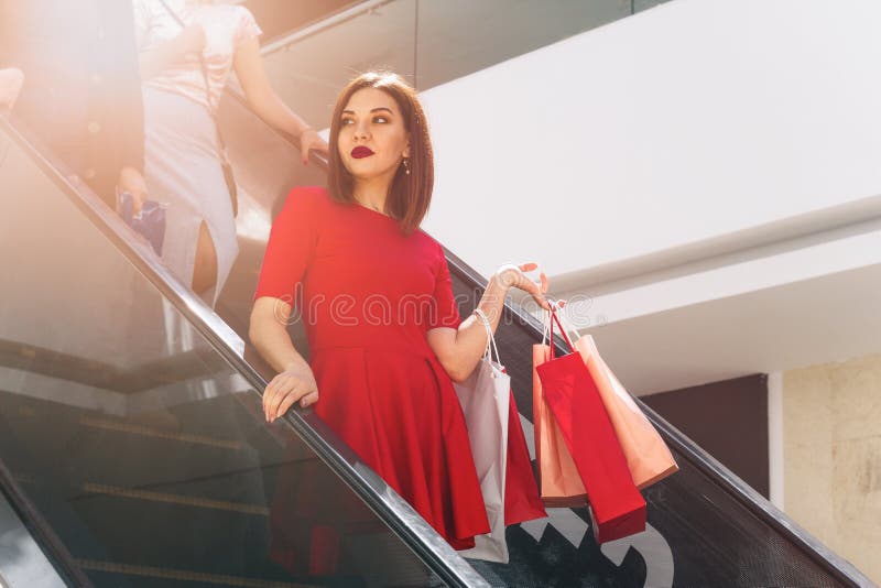 härlig brunett i röd klänning med shoppingpåsar som ner kommer shoppinggalleriarulltrappan arkivbilder härlig brunett i röd klänning med shoppingpåsar som ner kommer shoppinggalleriarulltrappan arkivbilder