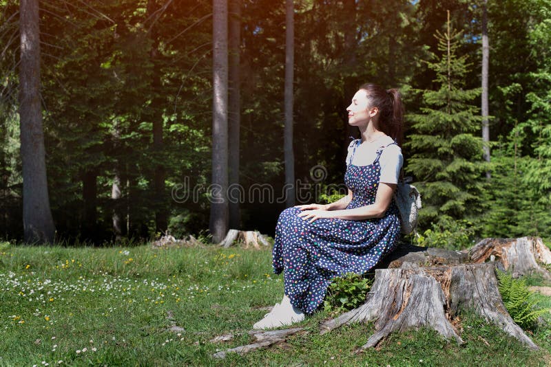 Härlig brunettflicka i en klänning som sitter på en stubbe på bakgrunden av en barrskog royaltyfria bilder Härlig brunettflicka i en klänning som sitter på en stubbe på bakgrunden av en barrskog royaltyfria bilder