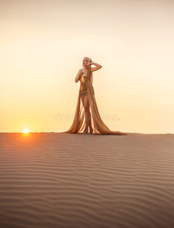 Beautiful queen of the desert at sunset walks. Luxury golden dress and unusual jewelry. Gold flower in her hair, hairstyle with braids. Beautiful blonde. Fashionable toning. Beautiful queen of the desert at sunset walks. Luxury golden dress and unusual jewelry. Gold flower in her hair, hairstyle with braids. Beautiful blonde. Fashionable toning.