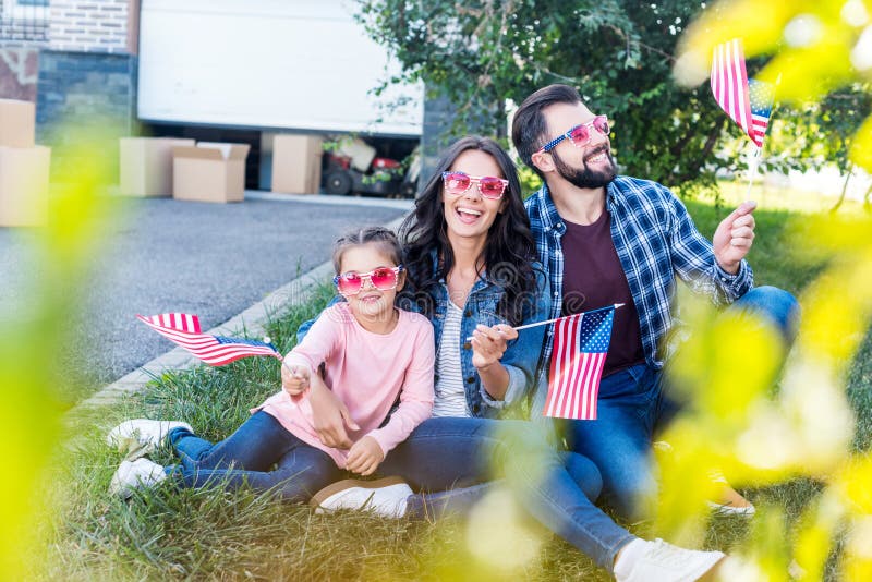 härlig familj med amerikanska flaggan och solglasögon som sitter i trädgård av royaltyfria bilder härlig familj med amerikanska flaggan och solglasögon som sitter i trädgård av royaltyfria bilder