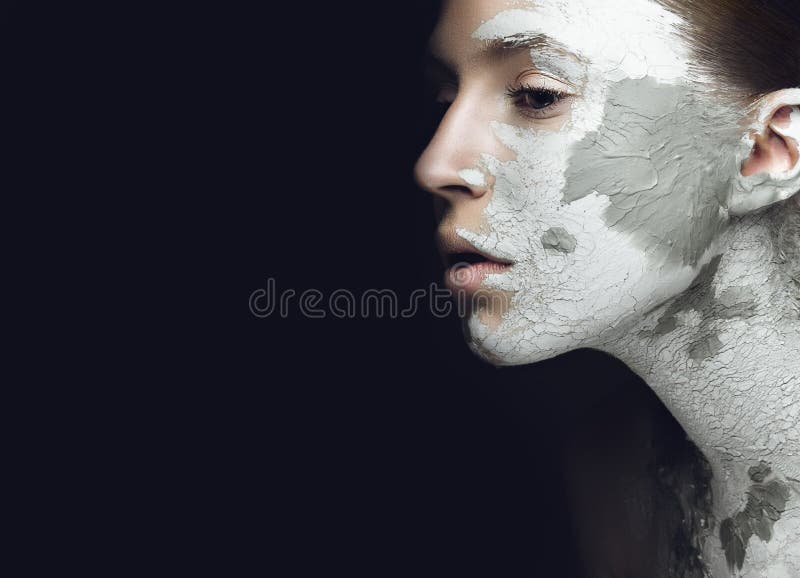 Beautiful girl with mud on his face. Cosmetic mask. Beauty face. Picture taken in the studio on a black background. Beautiful girl with mud on his face. Cosmetic mask. Beauty face. Picture taken in the studio on a black background.