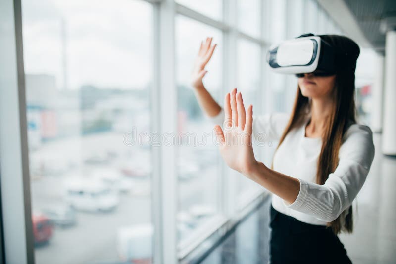 Härlig flicka som använder virtuell verklighetexponeringsglas nära ljust fönster med skyskrapasikt utanför Affärskvinna som bär V arkivbild Härlig flicka som använder virtuell verklighetexponeringsglas nära ljust fönster med skyskrapasikt utanför Affärskvinna som bär V arkivbild