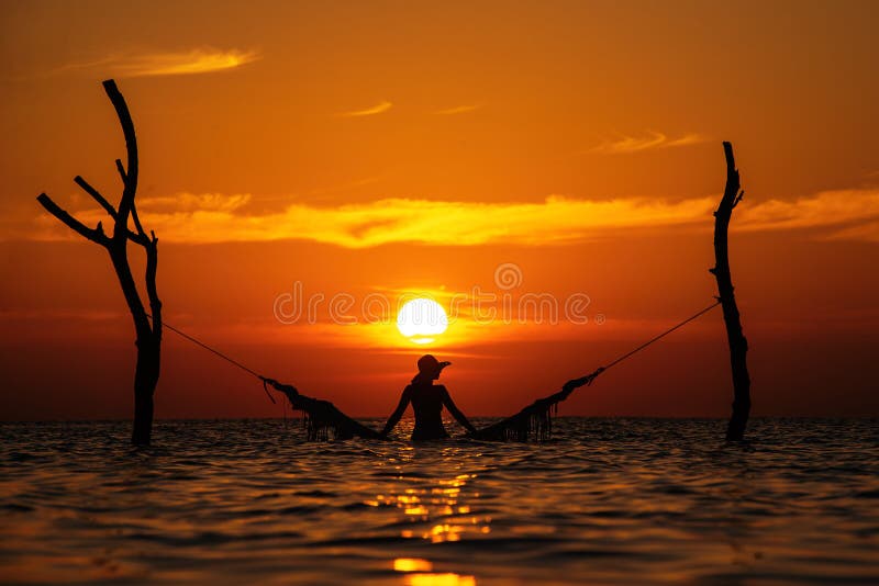 Härlig kontur för ung kvinna med gunga som poserar i havet på solnedgången, maldivian romantiskt landskap arkivfoto Härlig kontur för ung kvinna med gunga som poserar i havet på solnedgången, maldivian romantiskt landskap arkivfoto