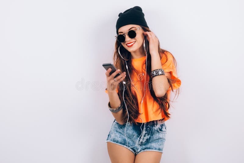 Härlig kvinna för ung hipster i solglasögon som nära bär i musik för T-tröja för svart hatt och apelsinlyssnande i hörlurar fotografering för bildbyråer Härlig kvinna för ung hipster i solglasögon som nära bär i musik för T-tröja för svart hatt och apelsinlyssnande i hörlurar fotografering för bildbyråer