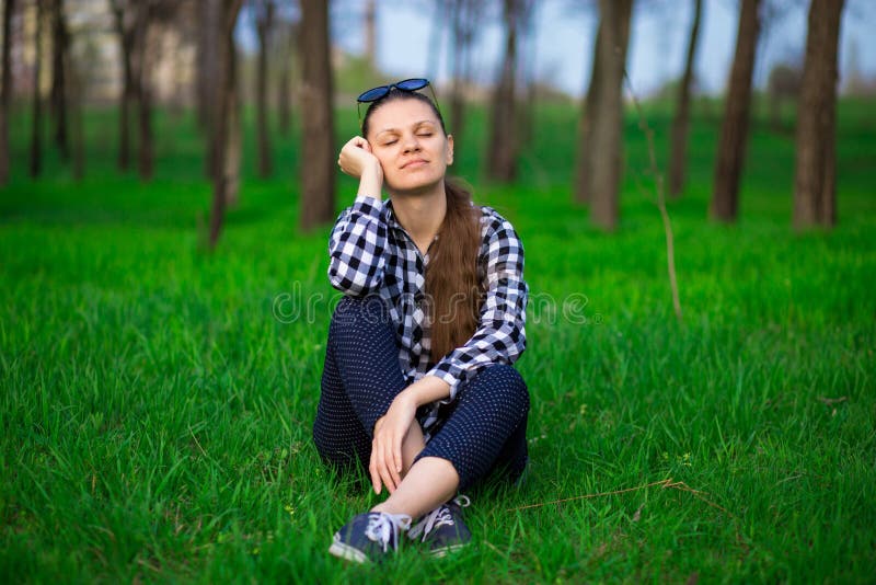 Härlig kvinna för ungt brunettanbud med stängda ögon som sitter på att koppla av för gräs fotografering för bildbyråer Härlig kvinna för ungt brunettanbud med stängda ögon som sitter på att koppla av för gräs fotografering för bildbyråer