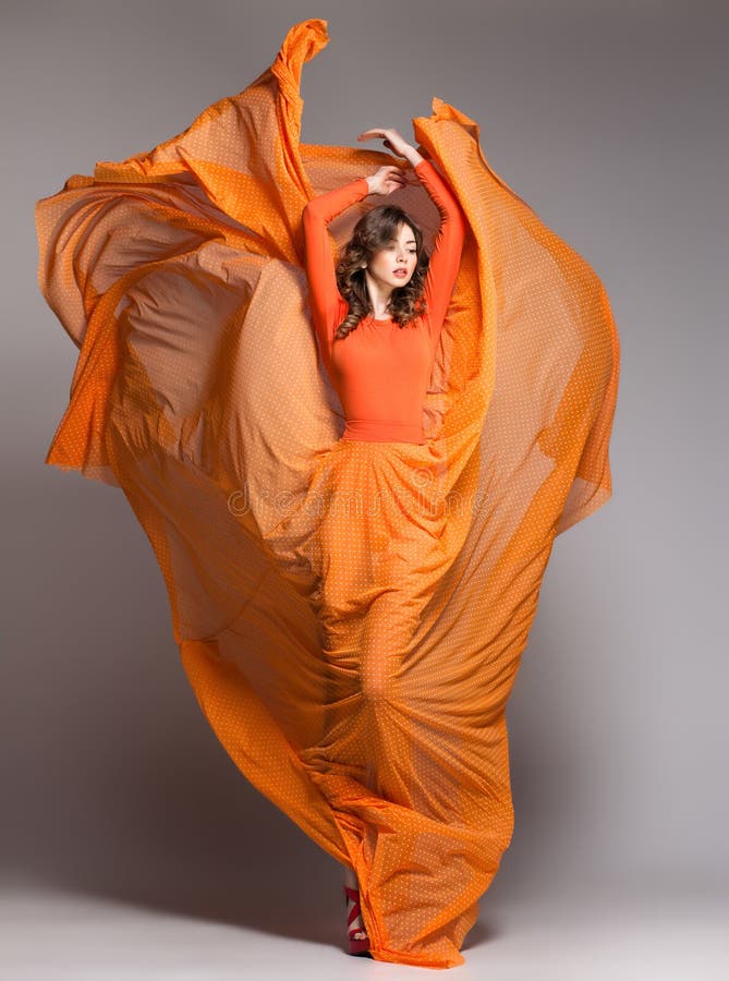 Härlig kvinna i långt orange posera för klänning som är dramatiskt
