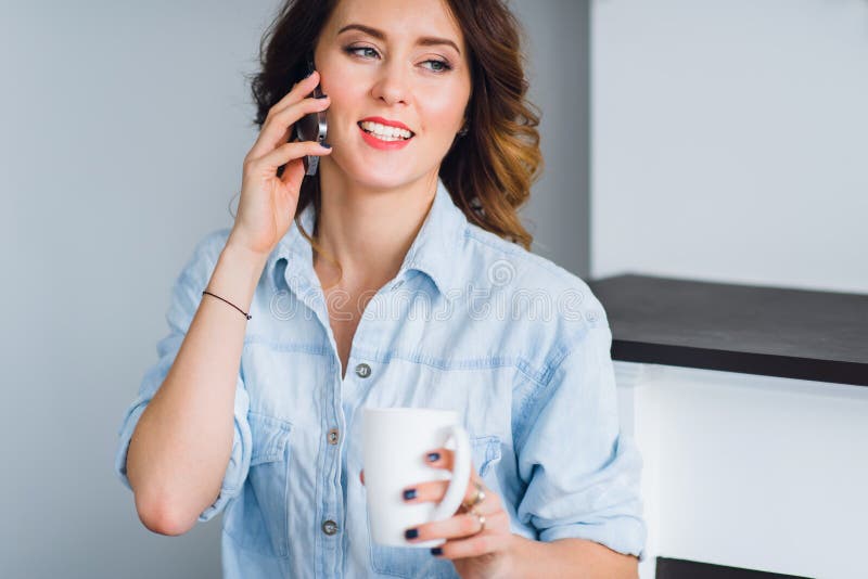 Härlig le kvinna med kaffekoppen som hemma talar på en mobiltelefon royaltyfri foto Härlig le kvinna med kaffekoppen som hemma talar på en mobiltelefon royaltyfri foto
