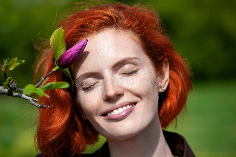Härlig le röd haired flicka med stängda ögon tycka om mjukheten av magnolian för blommaknopp f inomhus royaltyfria foton Härlig le röd haired flicka med stängda ögon tycka om mjukheten av magnolian för blommaknopp f inomhus royaltyfria foton