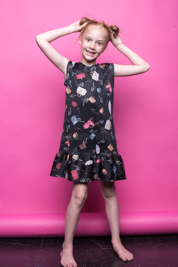 Härlig liten rödhårig manflicka i klänningen som poserar som modell på rosa bakgrund royaltyfri fotografi Härlig liten rödhårig manflicka i klänningen som poserar som modell på rosa bakgrund royaltyfri fotografi