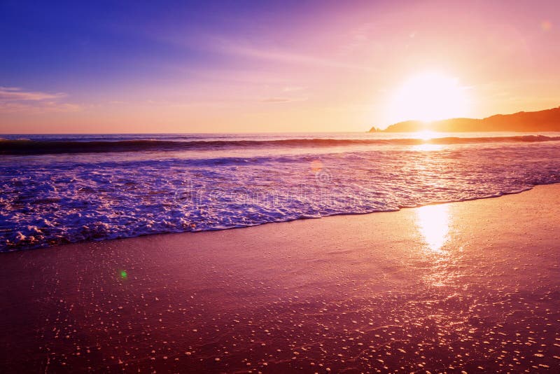 Beautiful bright purple purple sunset on the ocean, sandy beach, waves and glare of the sun. Beautiful bright purple purple sunset on the ocean, sandy beach, waves and glare of the sun