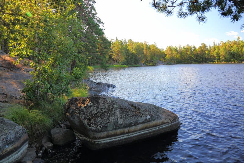 Härlig naturlandskapsikt Sjö med den steniga kustlinjen, yttersida för blått vatten och gräsplanträd på blå himmel fotografering för bildbyråer Härlig naturlandskapsikt Sjö med den steniga kustlinjen, yttersida för blått vatten och gräsplanträd på blå himmel fotografering för bildbyråer