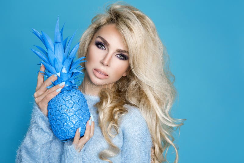 Härlig sexig blond kvinna för stående i blå tröja och innehav en blå ananas