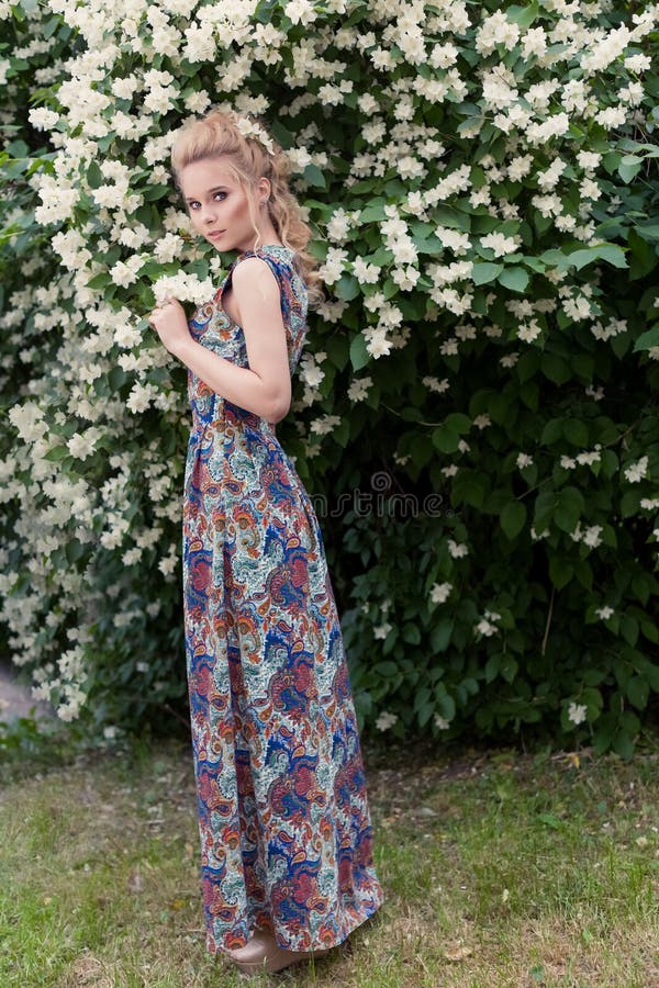 Härlig sexig mjuk blond flicka i en lång klänning med aftonfrisyranseende i trädgården nära ett aromatiskt träd för blomning royaltyfri foto Härlig sexig mjuk blond flicka i en lång klänning med aftonfrisyranseende i trädgården nära ett aromatiskt träd för blomning royaltyfri foto