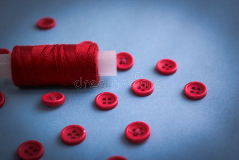 Härlig textur med massor av runda röda knappar för att sy, handarbete och en spole av tråden kopiera avstånd Lekmanna- blå bakgru royaltyfri bild Härlig textur med massor av runda röda knappar för att sy, handarbete och en spole av tråden kopiera avstånd Lekmanna- blå bakgru royaltyfri bild