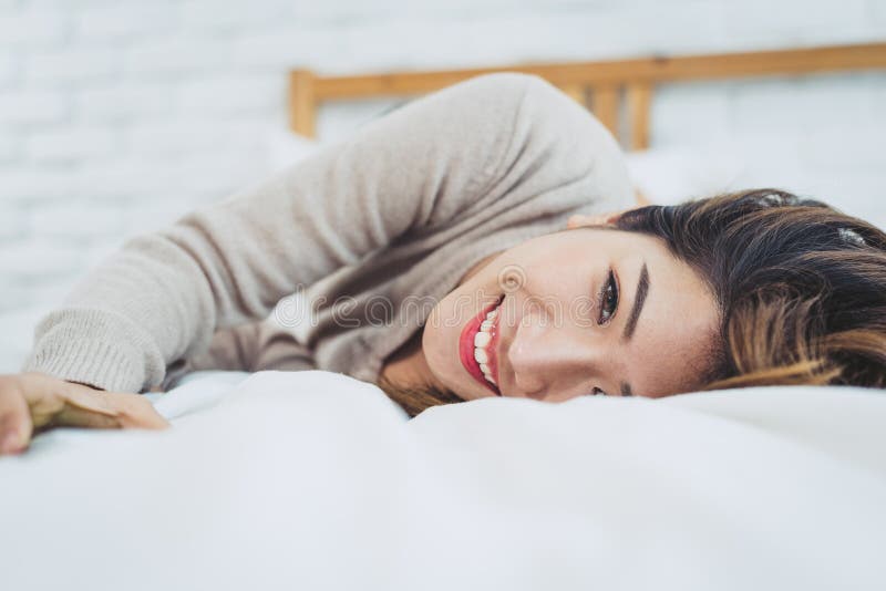 Härlig ung asiatisk kvinna för stående på säng hemma i morgonen Gladlynt asiatisk kvinna som bär en bekväm tröja och ler på hennes säng avslappnande lokal hemmastatt begrepp för livsstilasia kvinna