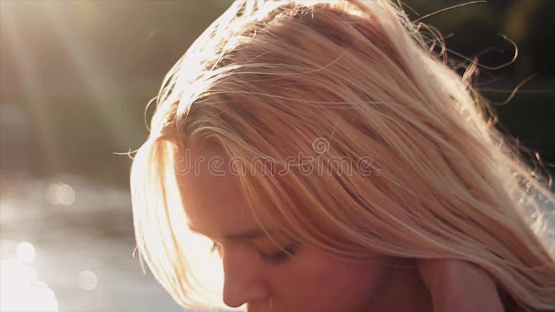 Härlig ung caucasian flicka som framme spelar med hennes blonda hår på solnedgång av vatten Stående Slowmotion