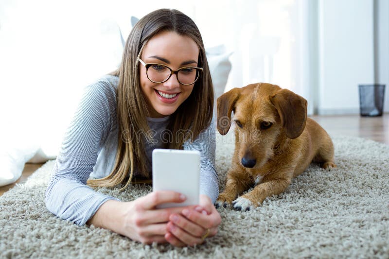 Härlig ung kvinna med hennes hund genom att använda mobiltelefonen hemma royaltyfri foto