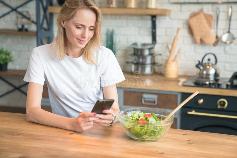 Härlig ung kvinna som använder mobiltelefonen, medan göra sallad i köket sund mat t?t sallad som skjutas upp gr?nsaken banta Sund royaltyfria bilder Härlig ung kvinna som använder mobiltelefonen, medan göra sallad i köket sund mat t?t sallad som skjutas upp gr?nsaken banta Sund royaltyfria bilder