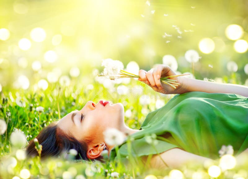 Härlig ung kvinna som ligger på fältet i grönt gräs och blåser maskrosblommor