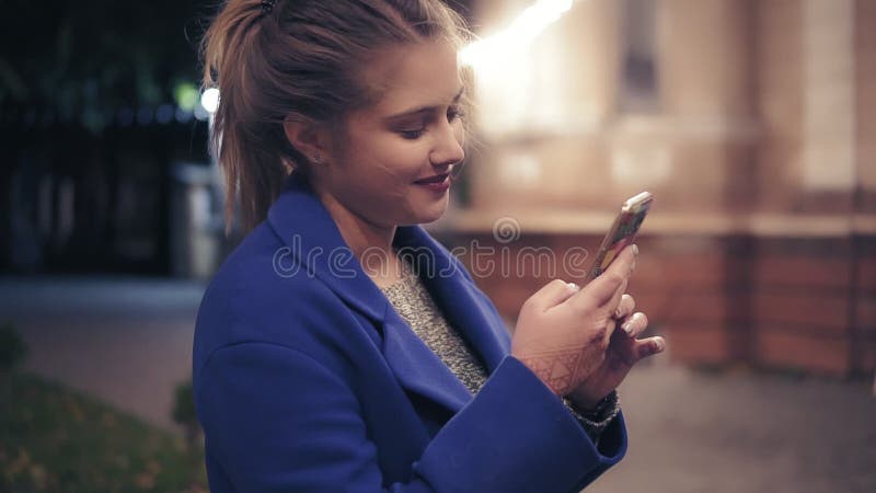 Härlig ung kvinna som sent använder hennes smarta telefon på natten i staden Attraktivt smsa för flicka som surfar på internet