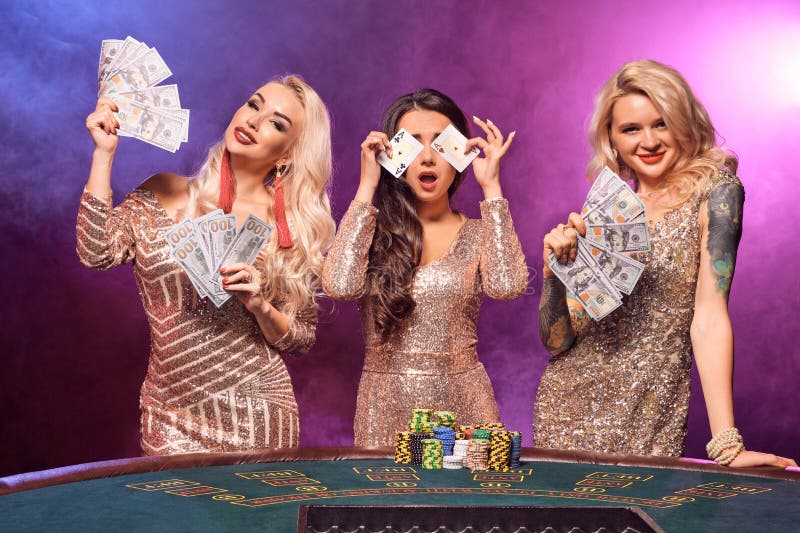 Härliga flickor med perfekta frisyrer och det ljusa sminket poserar anseende på en spela tabell Kasino poker royaltyfri foto Härliga flickor med perfekta frisyrer och det ljusa sminket poserar anseende på en spela tabell Kasino poker royaltyfri foto