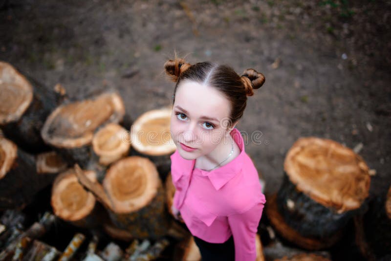 Härligt anseende för ung kvinna och se kameran på bunten av avverkade trädstammar i skogen arkivfoto Härligt anseende för ung kvinna och se kameran på bunten av avverkade trädstammar i skogen arkivfoto