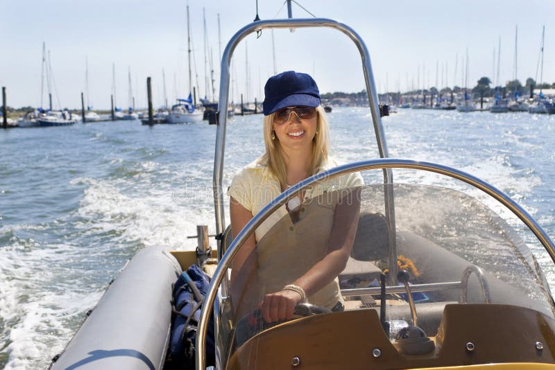 A stunningly beautiful young woman having fun driving a speedboat with moored sailing boats in the background. A stunningly beautiful young woman having fun driving a speedboat with moored sailing boats in the background