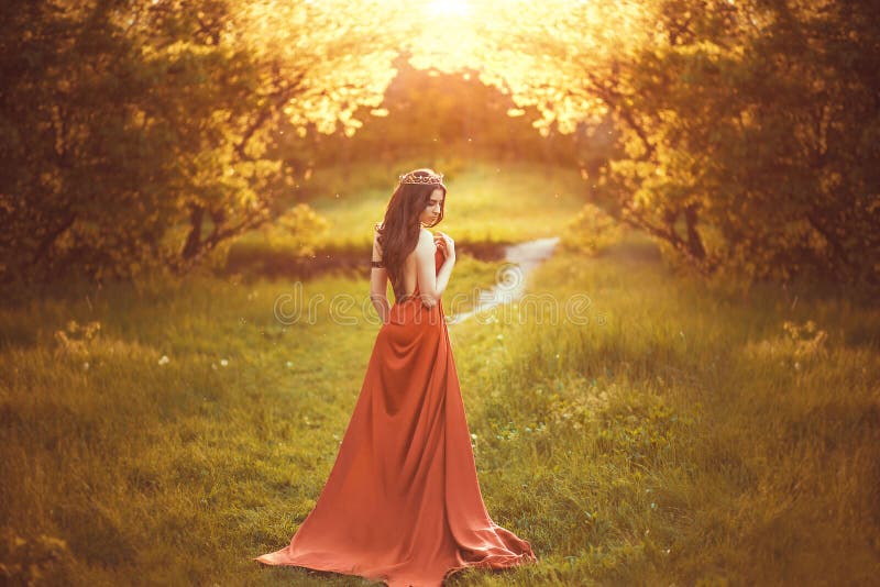 NBeautiful young princess in a long red dress walks among the green plants in the woods , a fashionable toning , creative color. NBeautiful young princess in a long red dress walks among the green plants in the woods , a fashionable toning , creative color