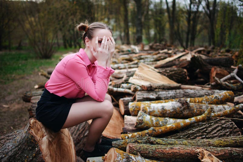 Härligt sammanträde och beläggning för ung kvinna hans framsida med hans händer, på bunten av avverkade trädstammar i skogen arkivfoton Härligt sammanträde och beläggning för ung kvinna hans framsida med hans händer, på bunten av avverkade trädstammar i skogen arkivfoton