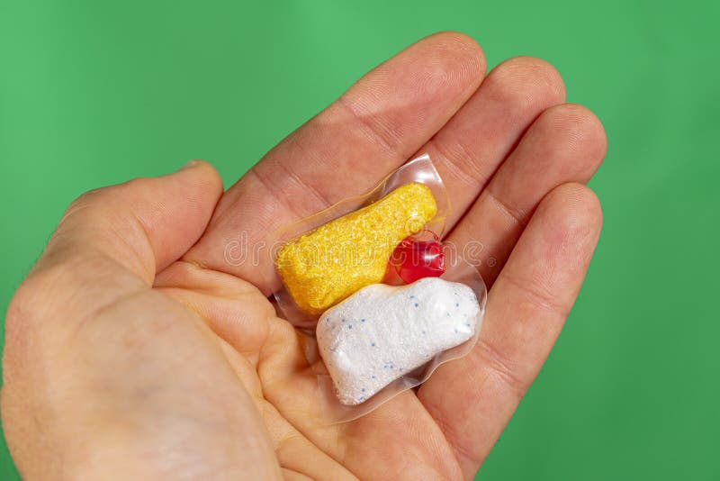 Håll i handflatan med diskmaskin- tabletten på grön bakgrund arkivfoton