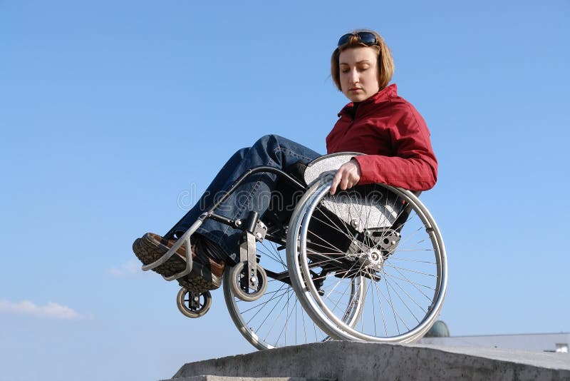 Wheelchair woman balancing by the concrete kerb over blue sky. Wheelchair woman balancing by the concrete kerb over blue sky