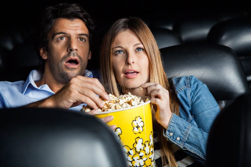 Hållande ögonen på film för chockade par i teater royaltyfria foton Hållande ögonen på film för chockade par i teater royaltyfria foton