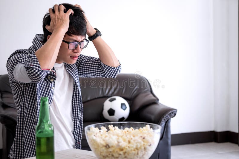 Hållande ögonen på fotbollsmatch för ung asiatisk manfanclub på tv och att hurra arkivbilder Hållande ögonen på fotbollsmatch för ung asiatisk manfanclub på tv och att hurra arkivbilder