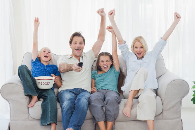 Hållande ögonen på television för familj och lyftaarmar arkivbild Hållande ögonen på television för familj och lyftaarmar arkivbild