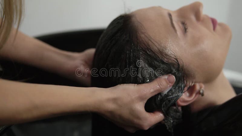 Hårfrisör tvättar en kvinna med lång halveringstid och masserar schampo i skåp före hårklippning Handtvättare